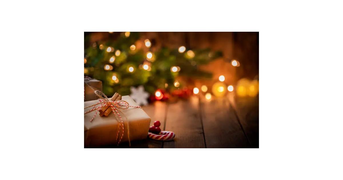 Wrapped gifts placed on a wooden table with a candy cane, in front of a Christmas tree decorated with dim lights in the background, creating a warm and festive atmosphere.