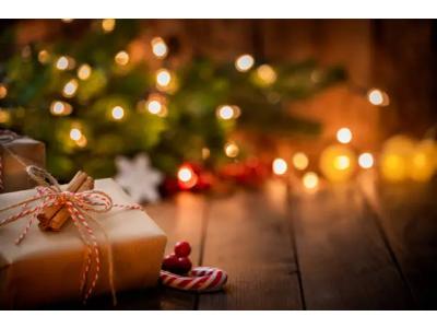 Wrapped gifts placed on a wooden table with a candy cane, in front of a Christmas tree decorated with dim lights in the background, creating a warm and festive atmosphere.